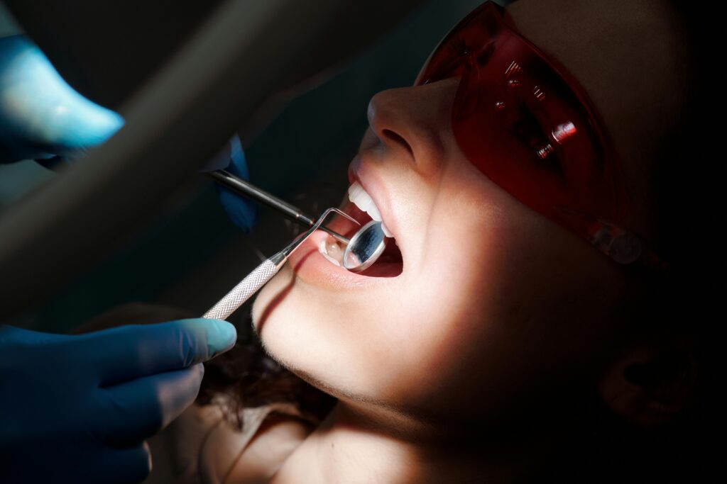 "how to choose the best dentist in varanasi for your smile"in 2025. A detailed close-up of a dental examination showing tools and a patient with protective eyewear.