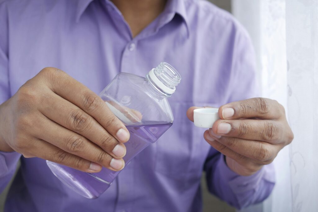 The Importance of Regular Use of best Toothpaste, Mouthwash in 2025. Close-up of hands holding a purple plastic bottle while pouring mouthwash into a cap.