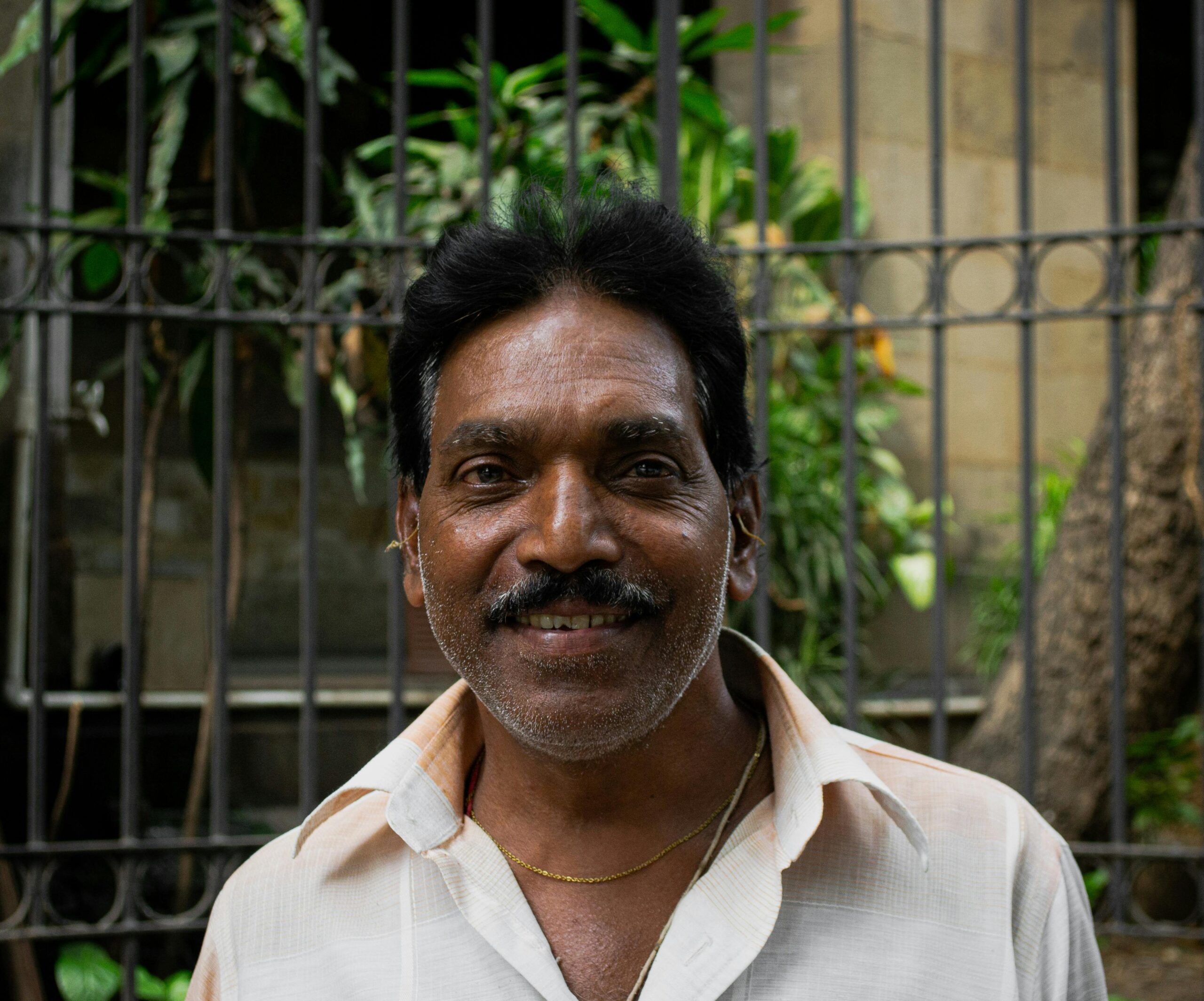 Portrait of a smiling senior Indian man outdoors by a decorative iron fence.