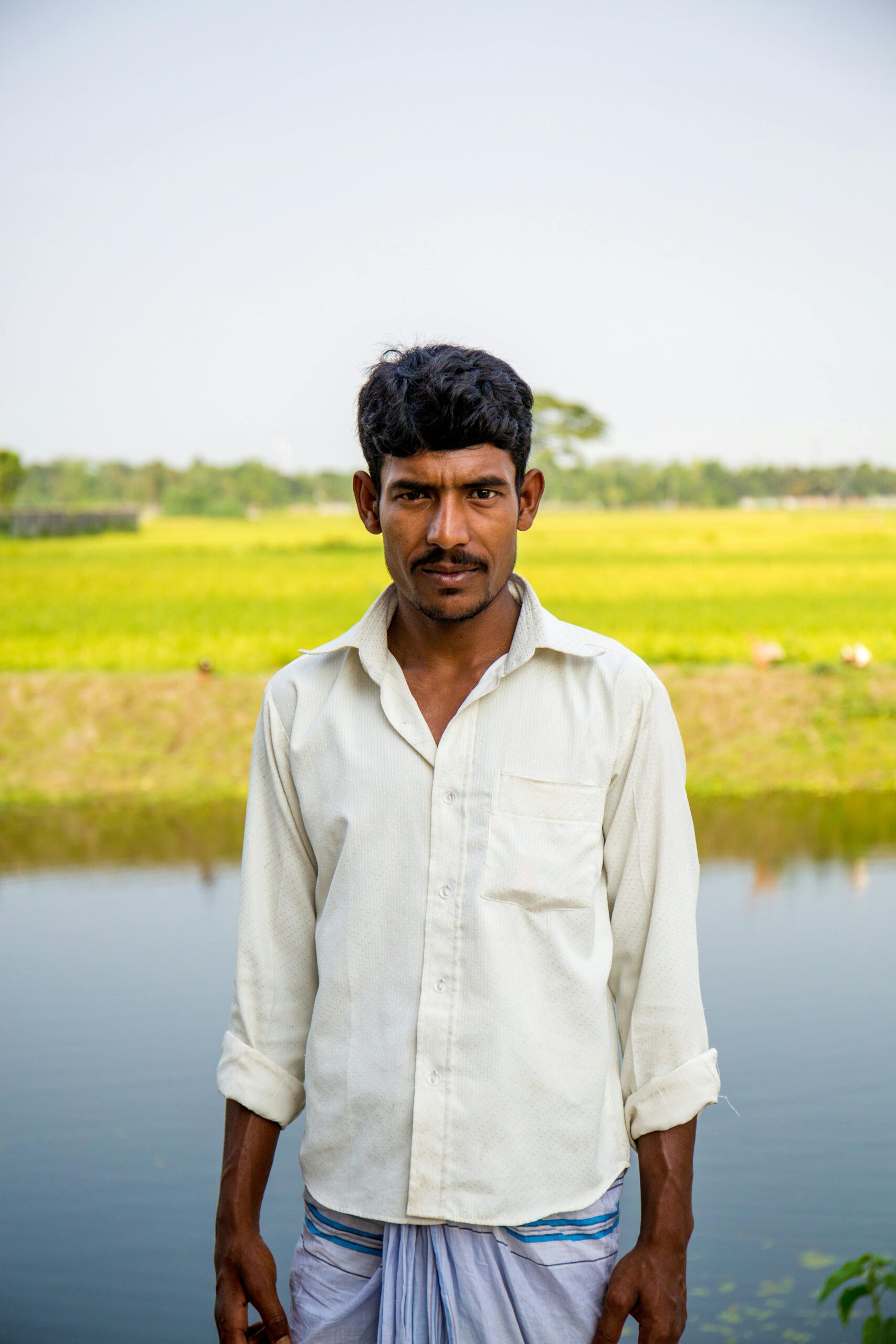 A portrait of a man standing near a pond in a rural countryside setting during summer.